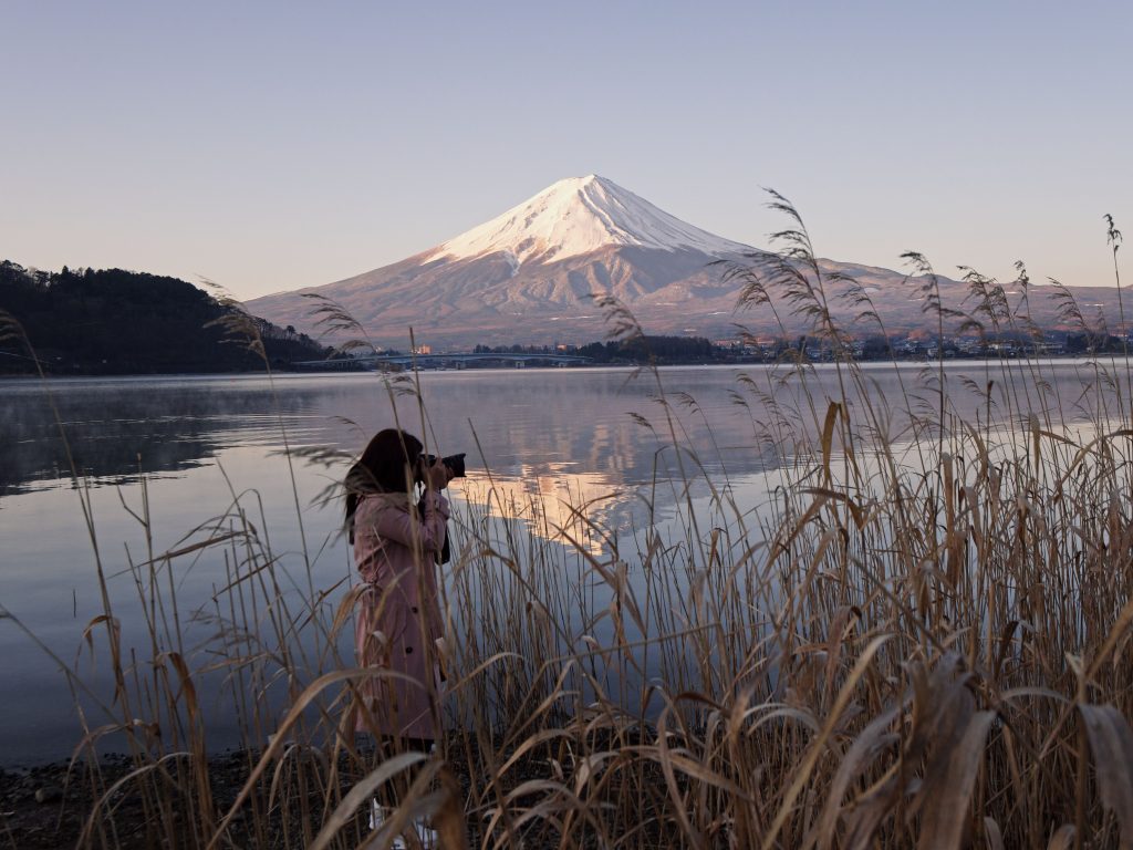 河口湖の岸辺で富士山を撮影する旅人（素材写真：Casia Charlie / Pexels）